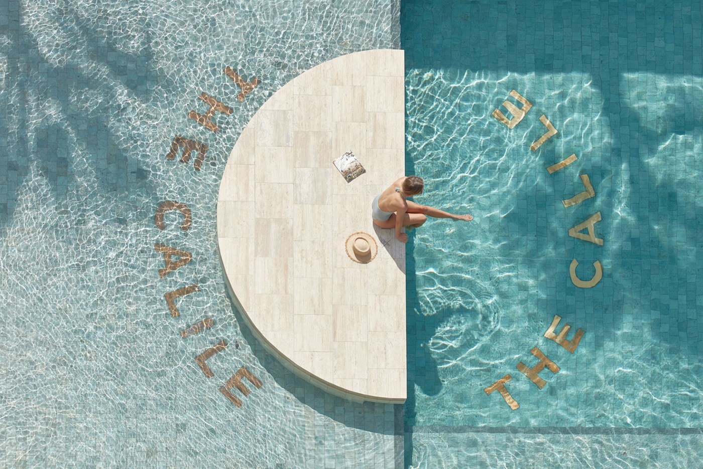 Bird eye view of the pool at The Calile Hotel, a person sits on the ledge kicking their feet