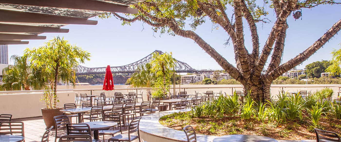 Exterior view of the deck at a riverside bar, with a view of the Story Bridge