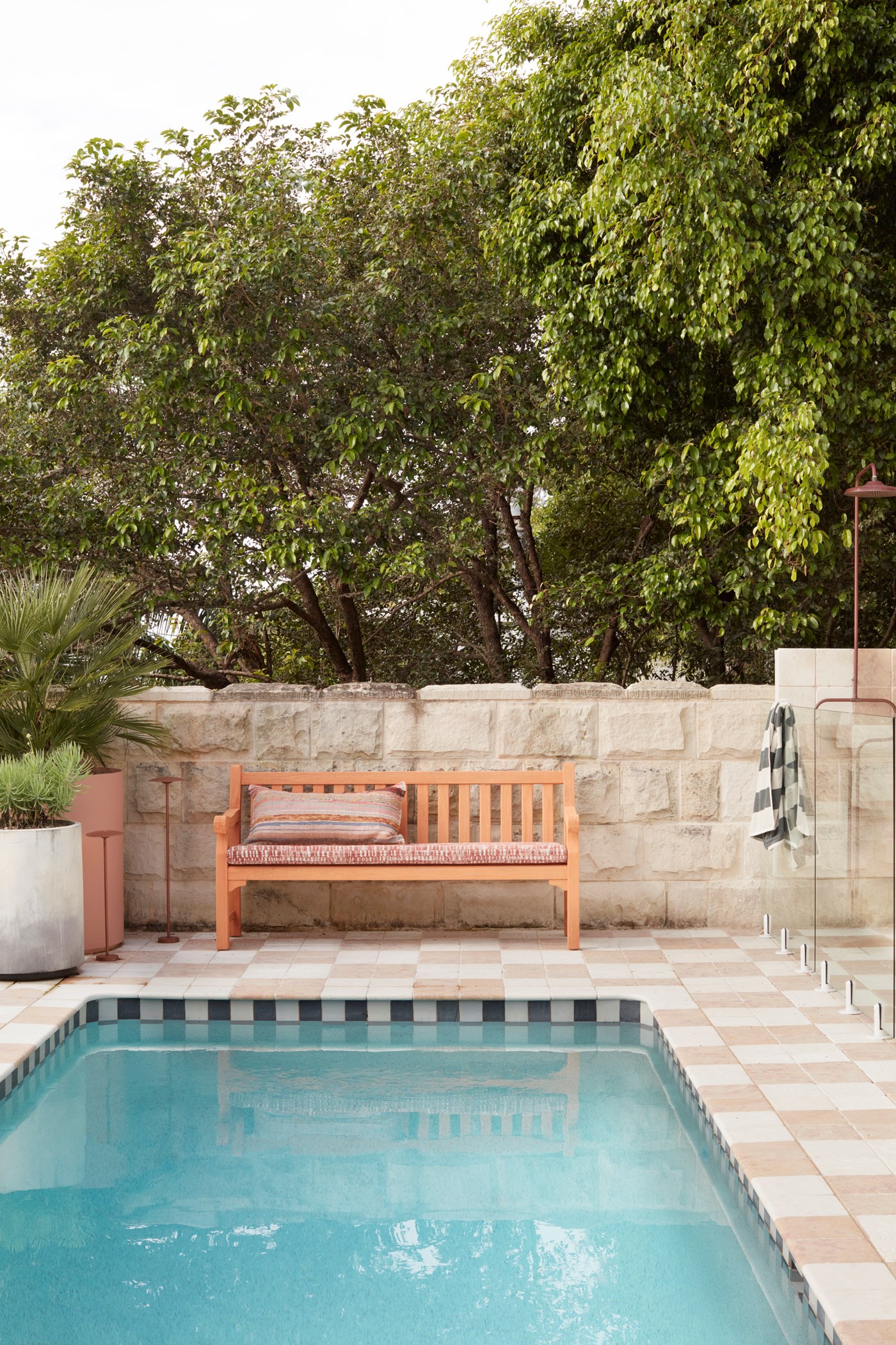 A pool is framed with chequered floors, a sandstone wall and an outdoor bench. 