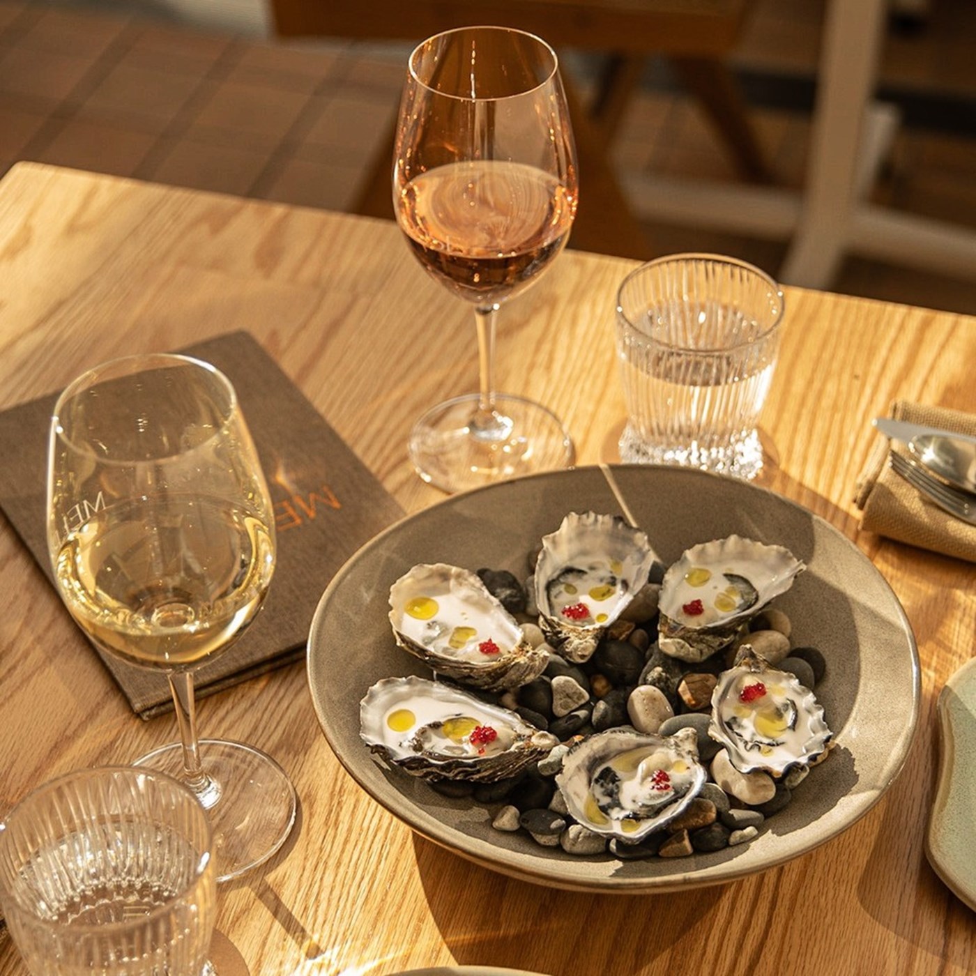 A sunlit table with two glasses and a plate of oysters