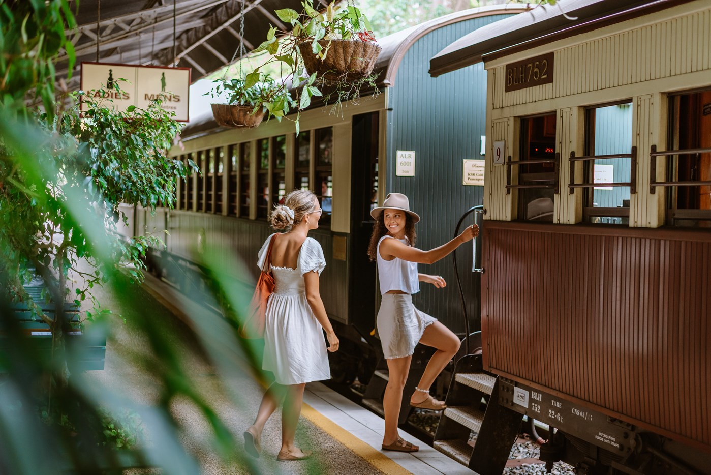 Two people stepping onto a vintage train at a leafy station