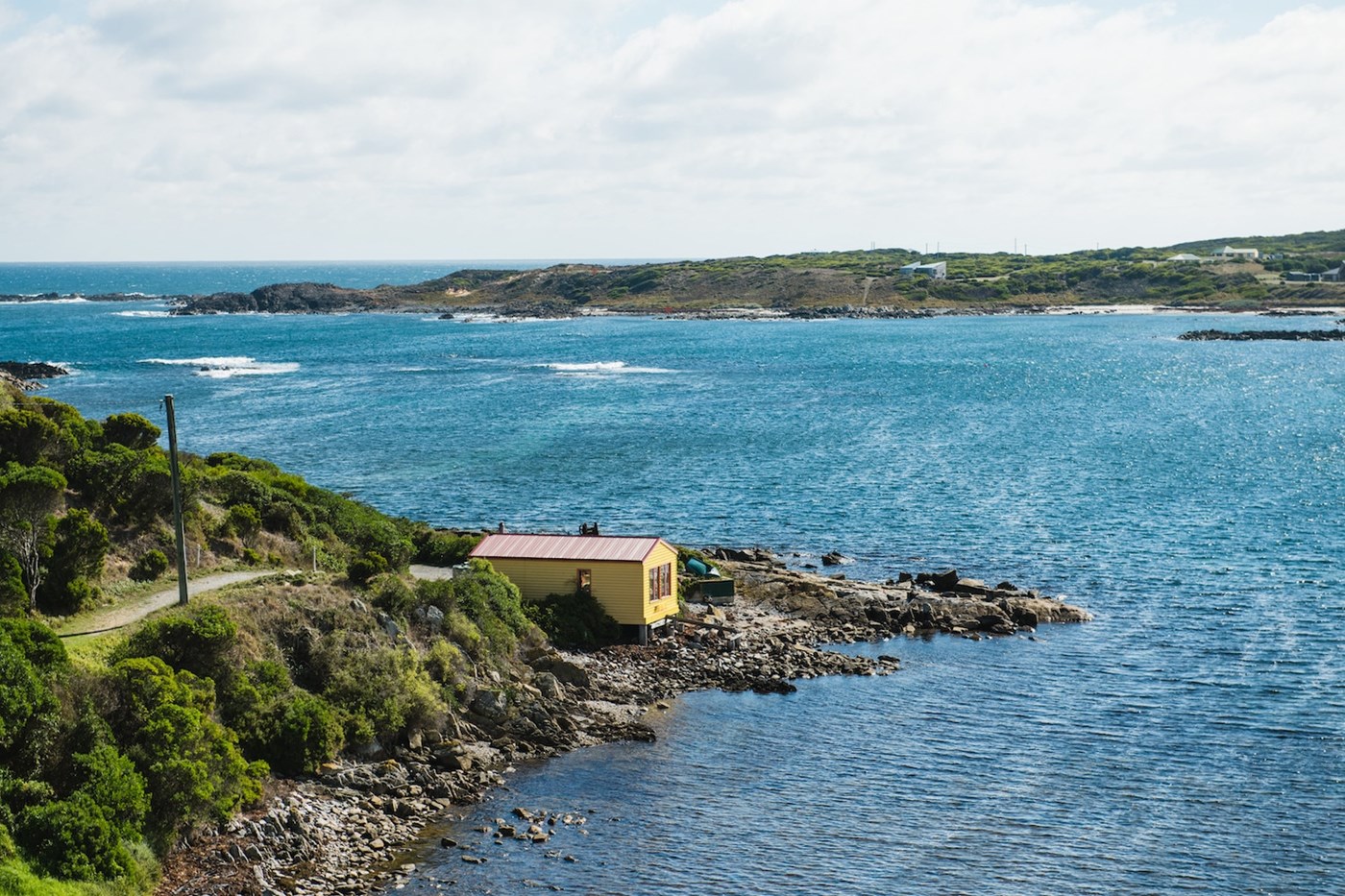 A small yellow shack on the end of a winding road, overlooking the ocean.