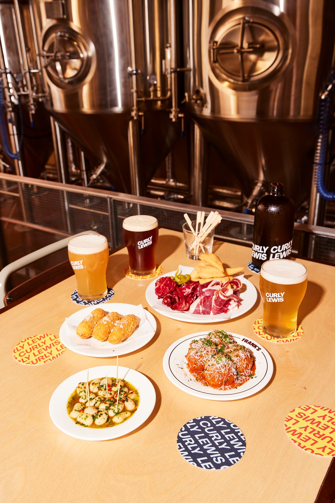 A selection of beers and snacks sitting on a table beside some of the vats of beers at Curly Lewis 