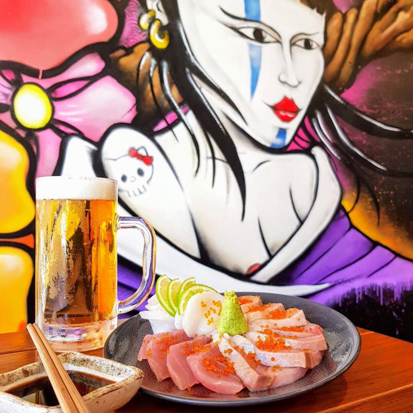 A pint of beer and plate of sashimi at Wawawa Izakaya, with a graffitied wall in the background.