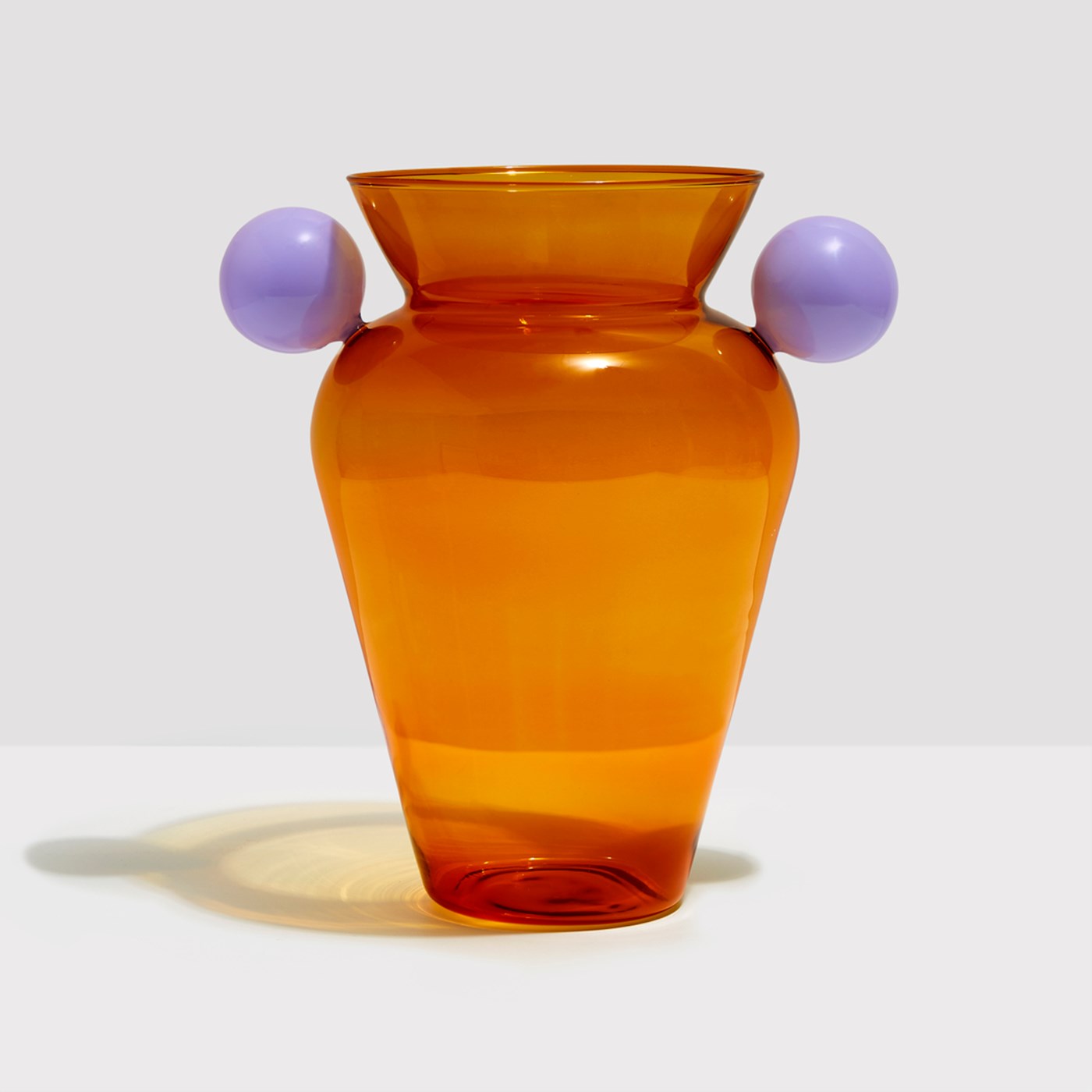 An urn shaped amber glass vase from Fazeek with a lilac sphere handle on either side 