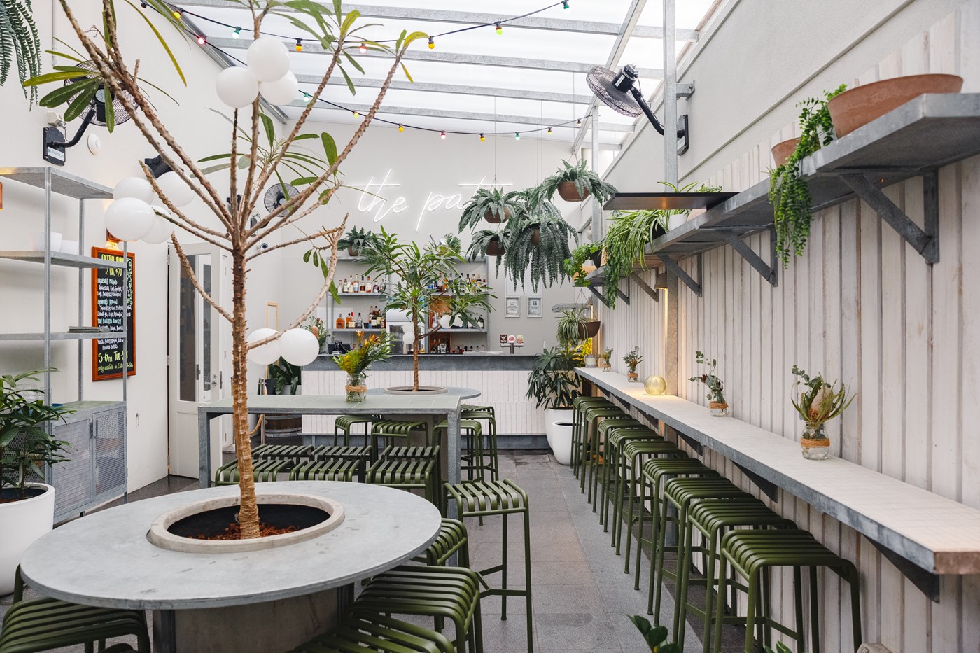 A bright, whitewashed interior featuring plants and green stools.