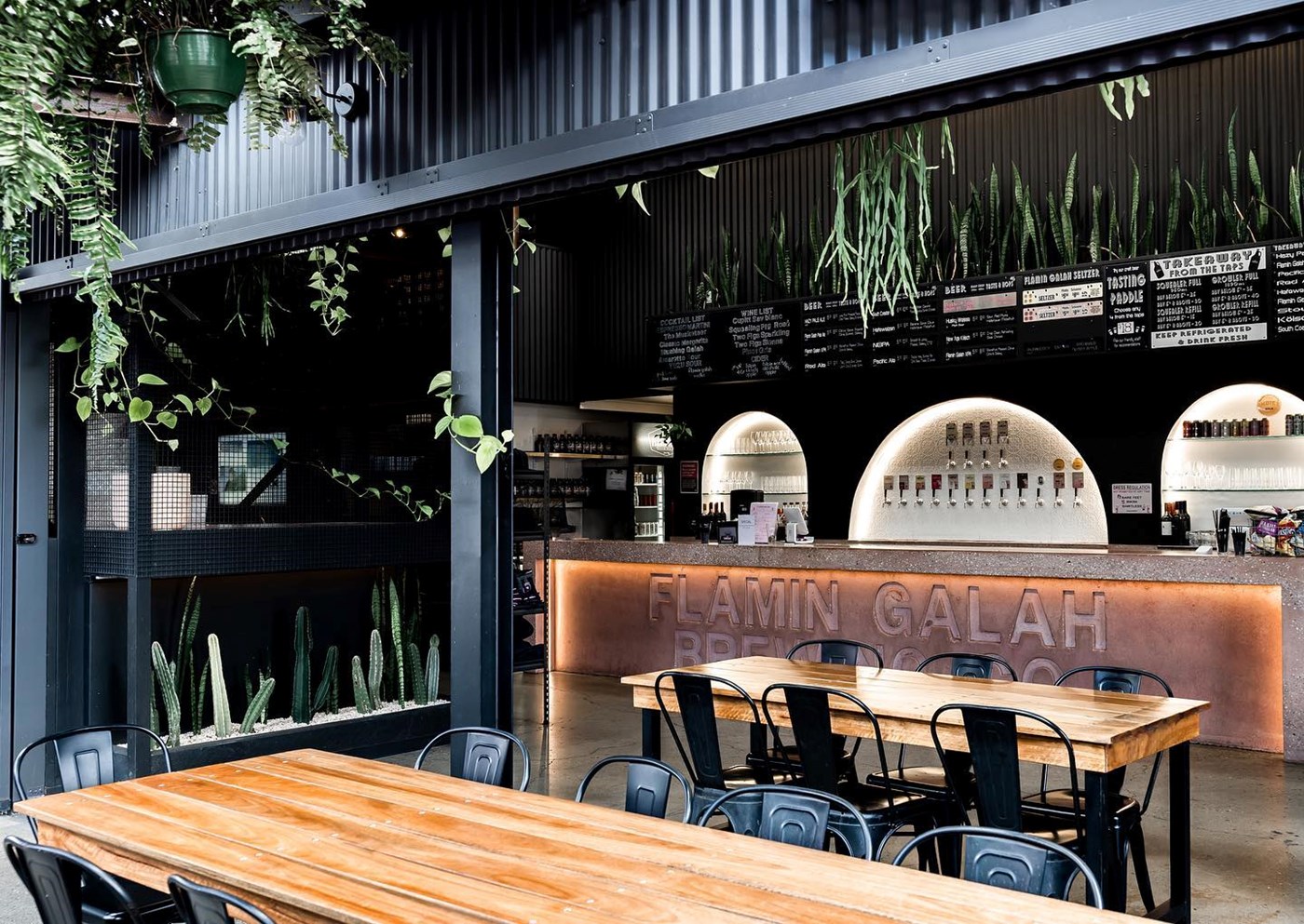 An industrial style tap room with black metal features, timber tables and lots of greenery 