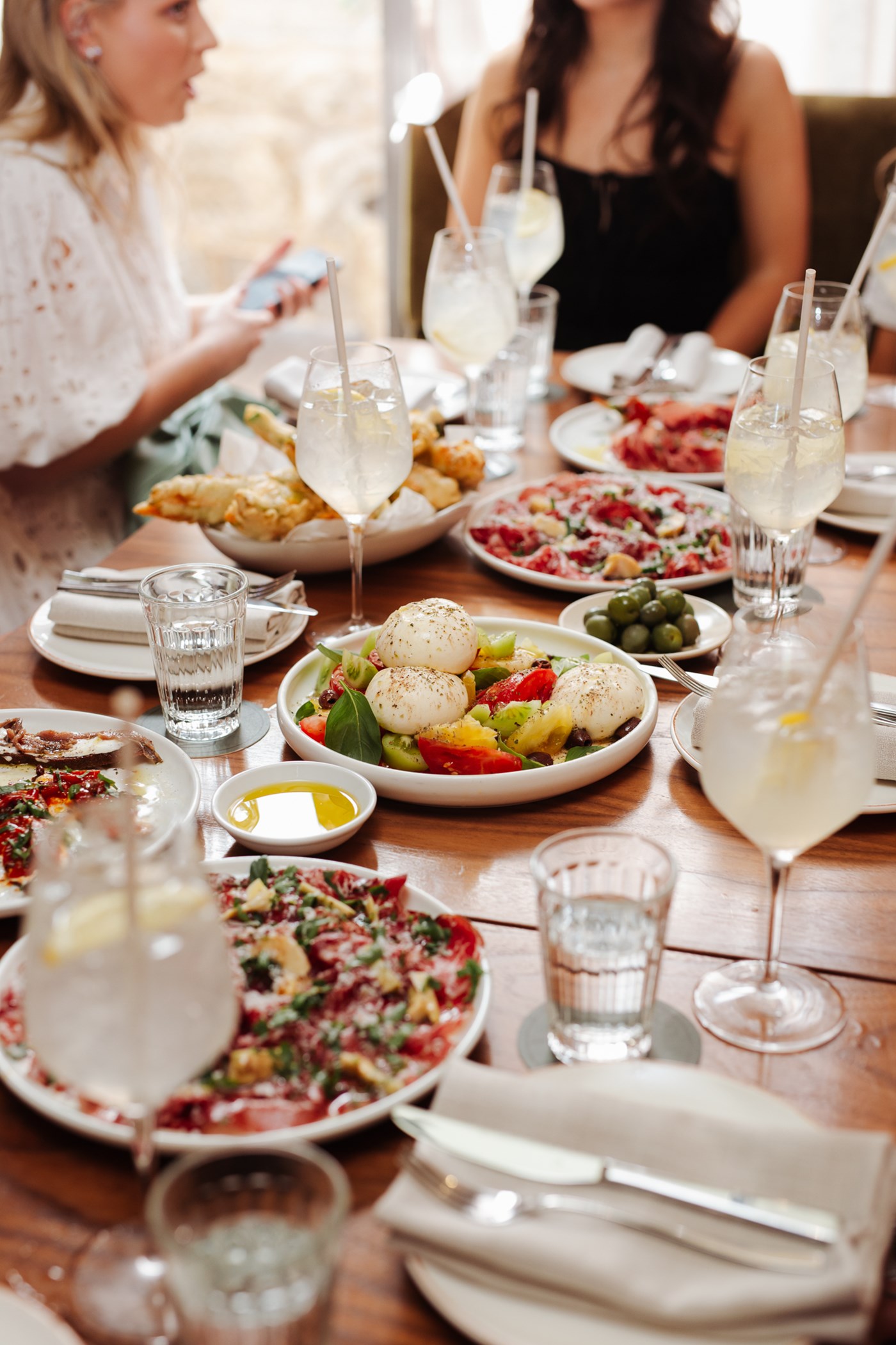 A table spread with cocktails, burrata, lives and other Italian dishes 