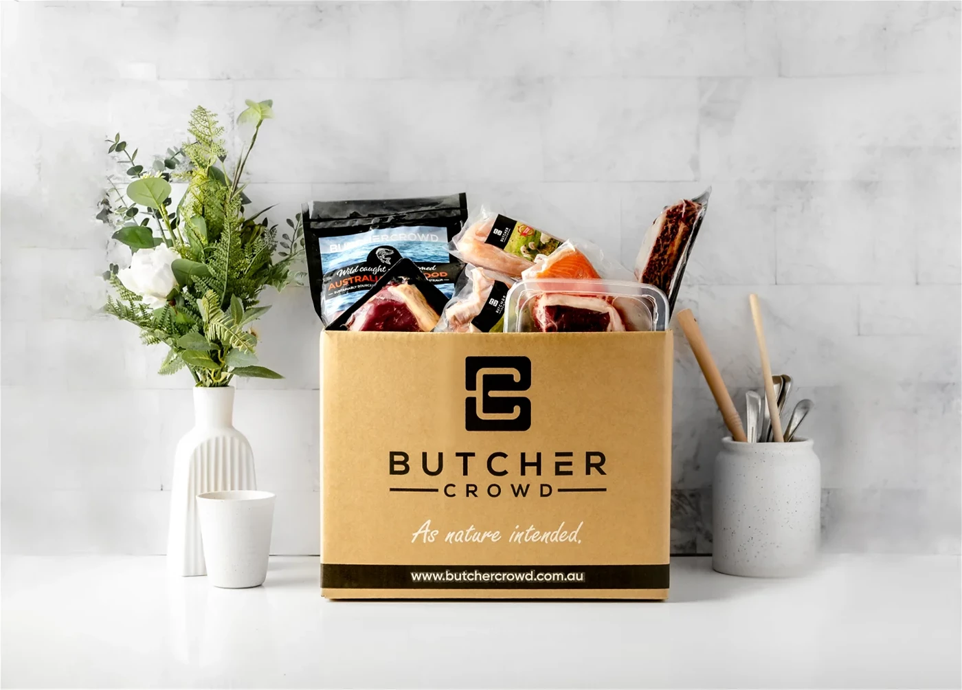 A box of meat and seafood from Butcher Crowd, places in a kitchen next to a vase of flowers,