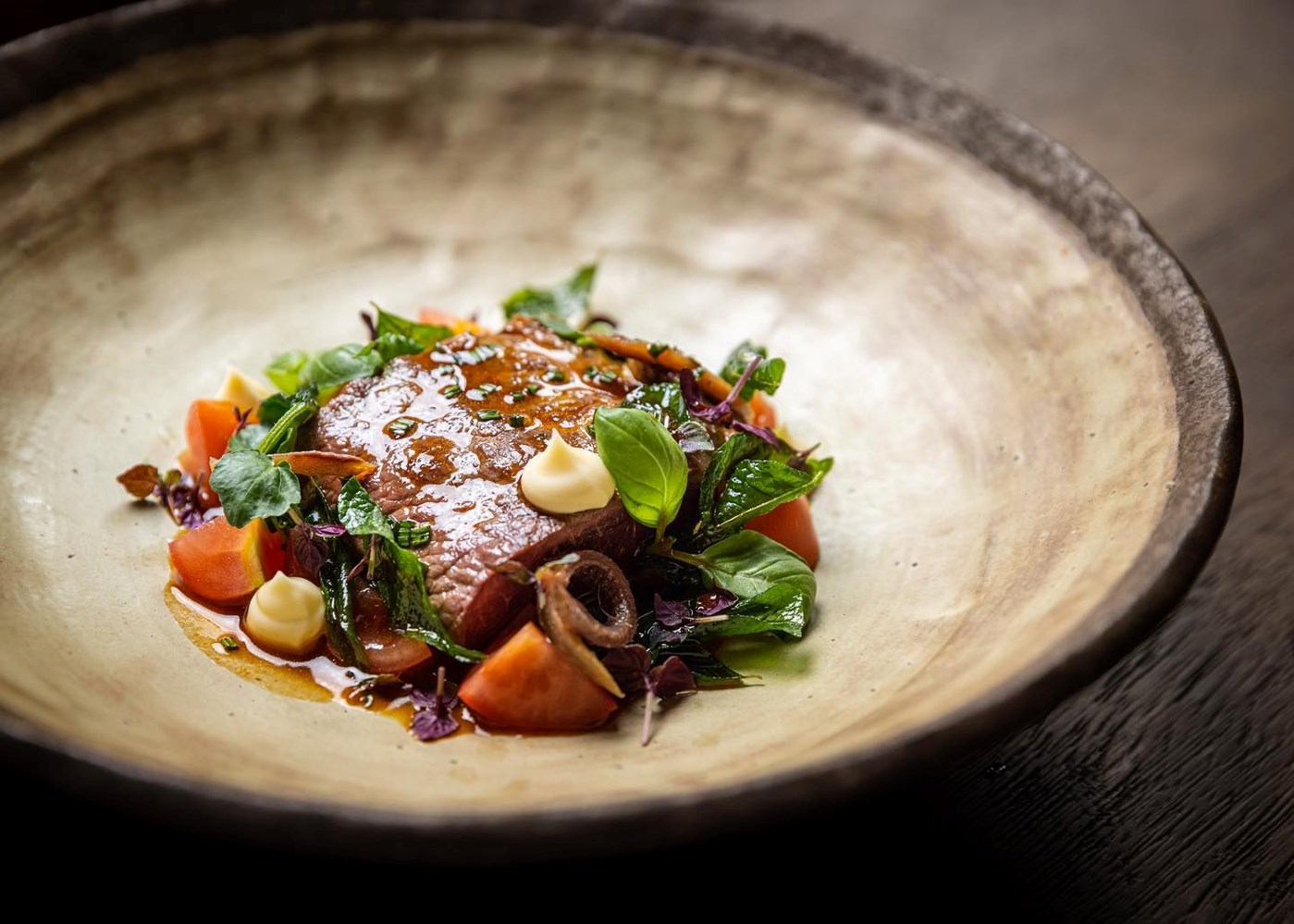 A beef main dish plated up with vegetables in a ceramic bowl at Otis Canberra. 