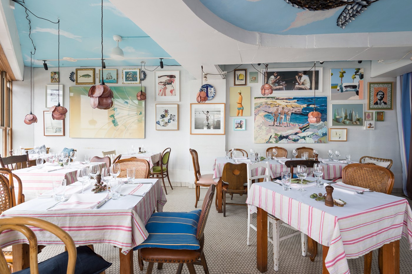 An eclectic dining room decked out with beachy and nautical paraphernalia. Tables are covered with red and white tablecloths 