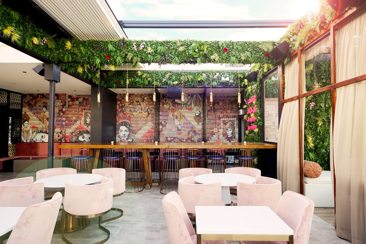 A rooftop bar with blush pink seats, hanging lanterns and curtains.