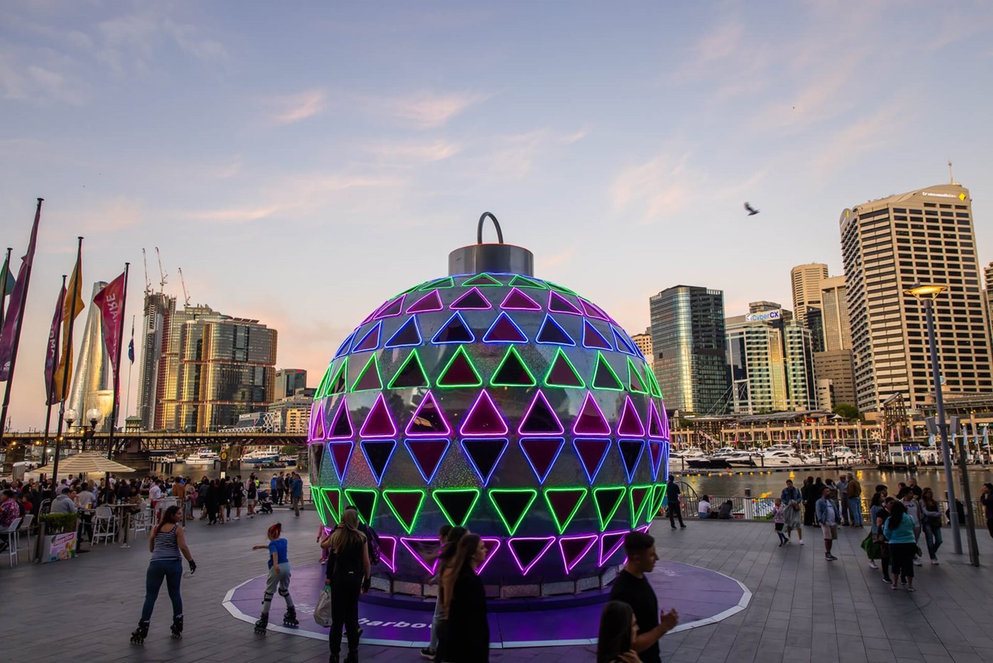 A giant six metre Christmas bauble illuminated with geometric patterns with the dusky city skyline in the background 