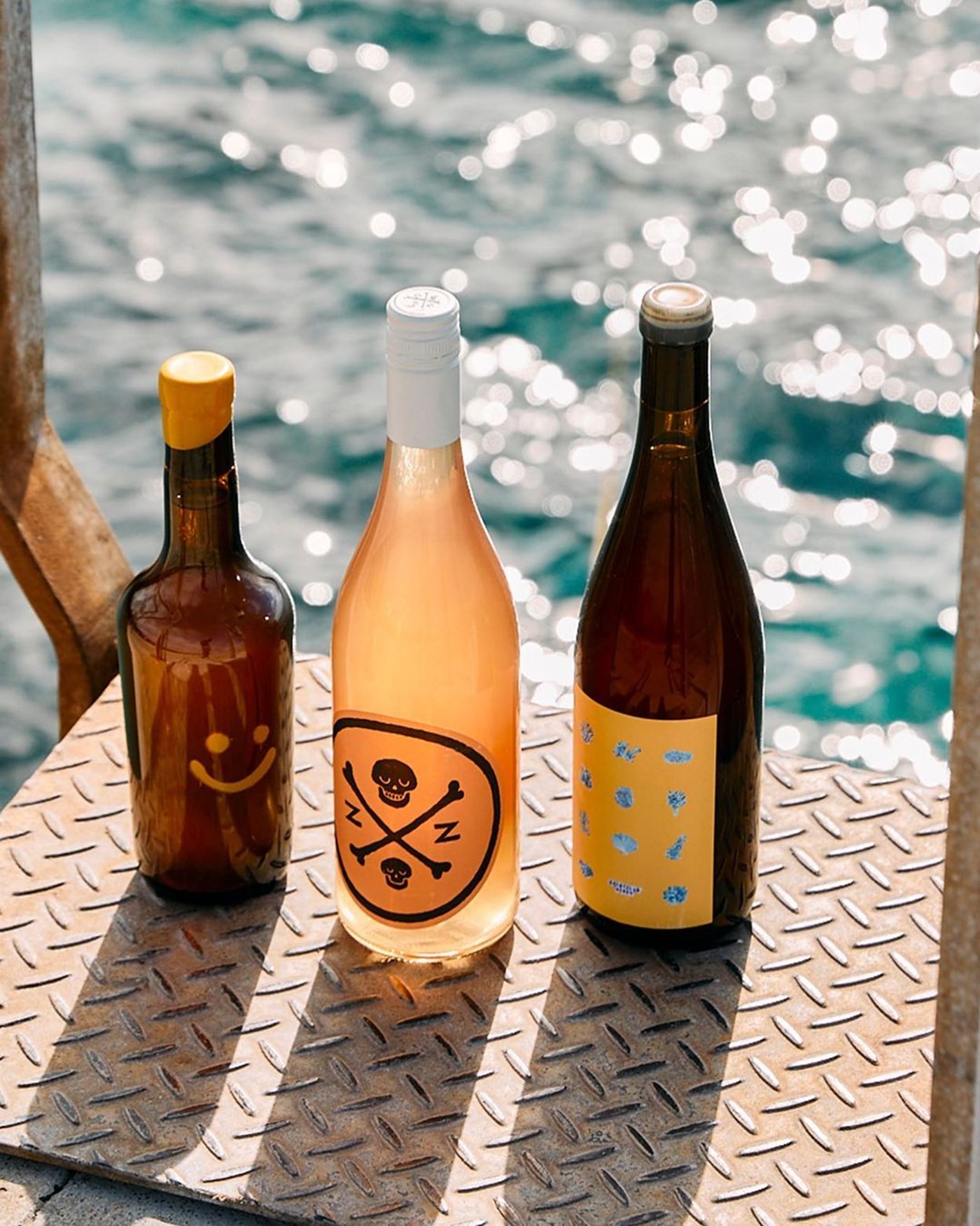 Three bottles of natural wines sitting on a metal grate with the ocean in the background
