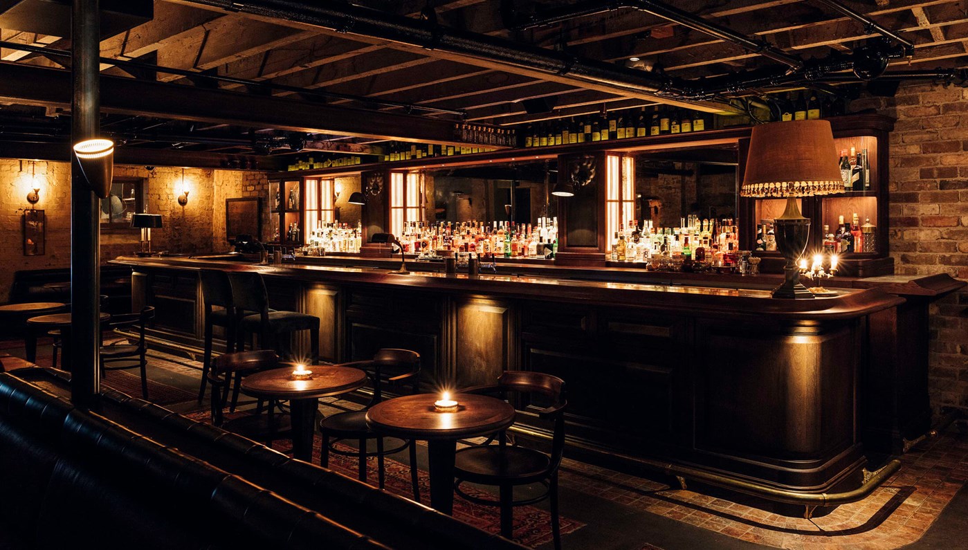A very moody and low lit bar with dark wooden furniture and large antique looking lamps 