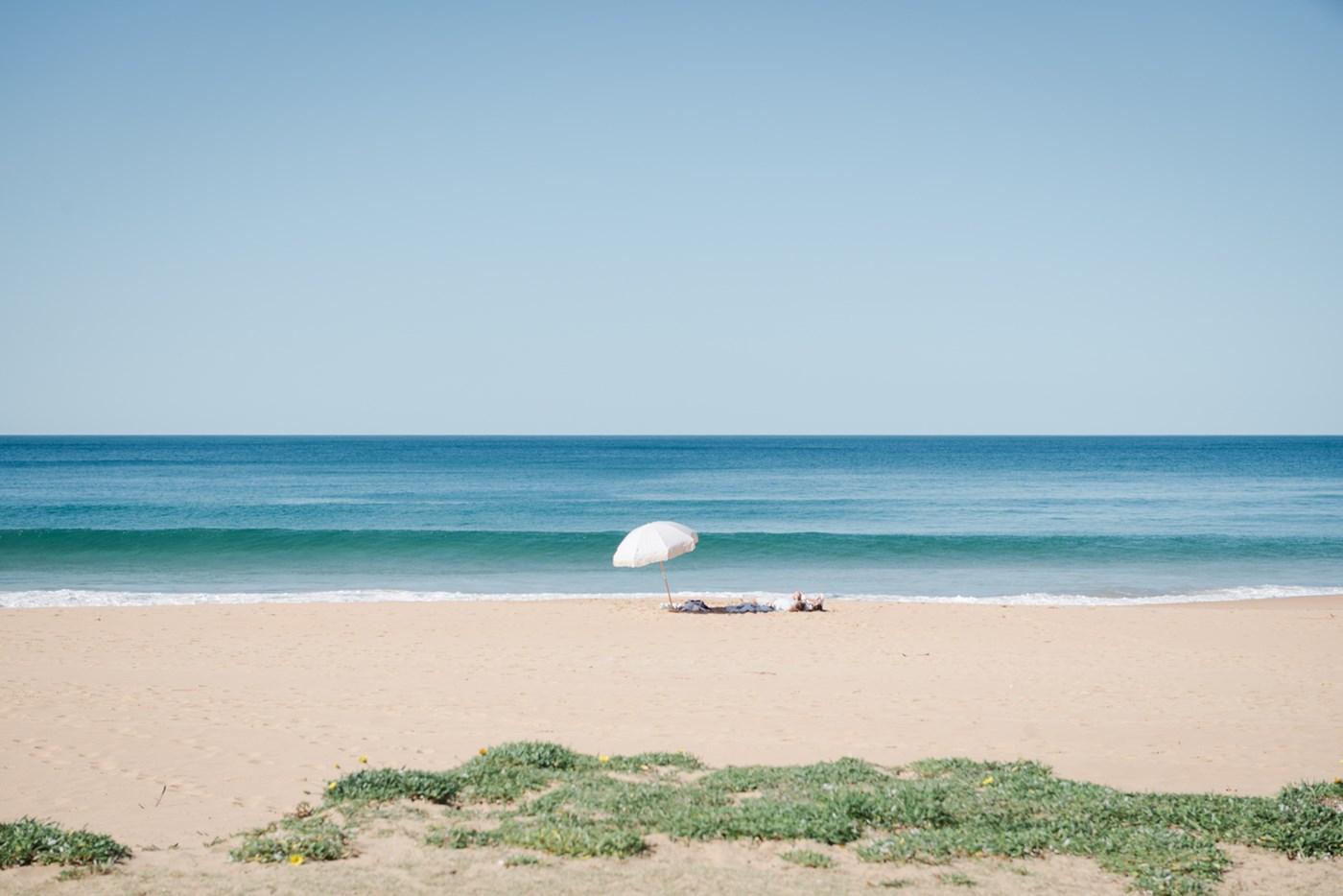 A lone beach umbrella and sunbather on the sand at Palm Beach NSW