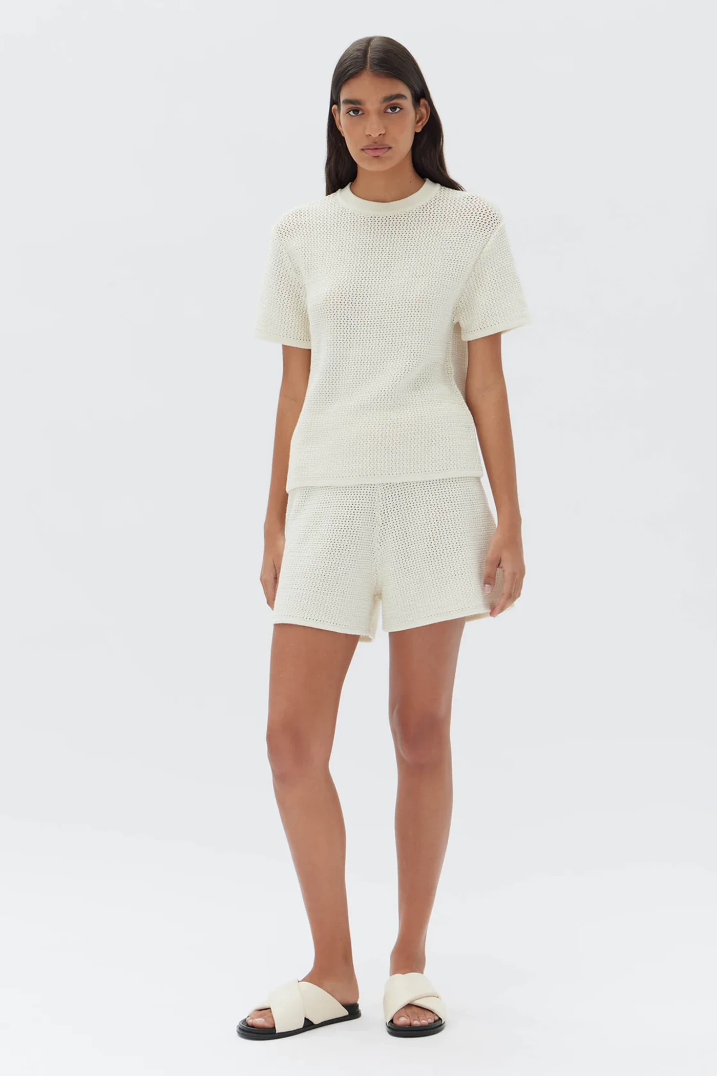 A woman wears a white crochet set in shorts and a T-shirt by the Assembly Label.