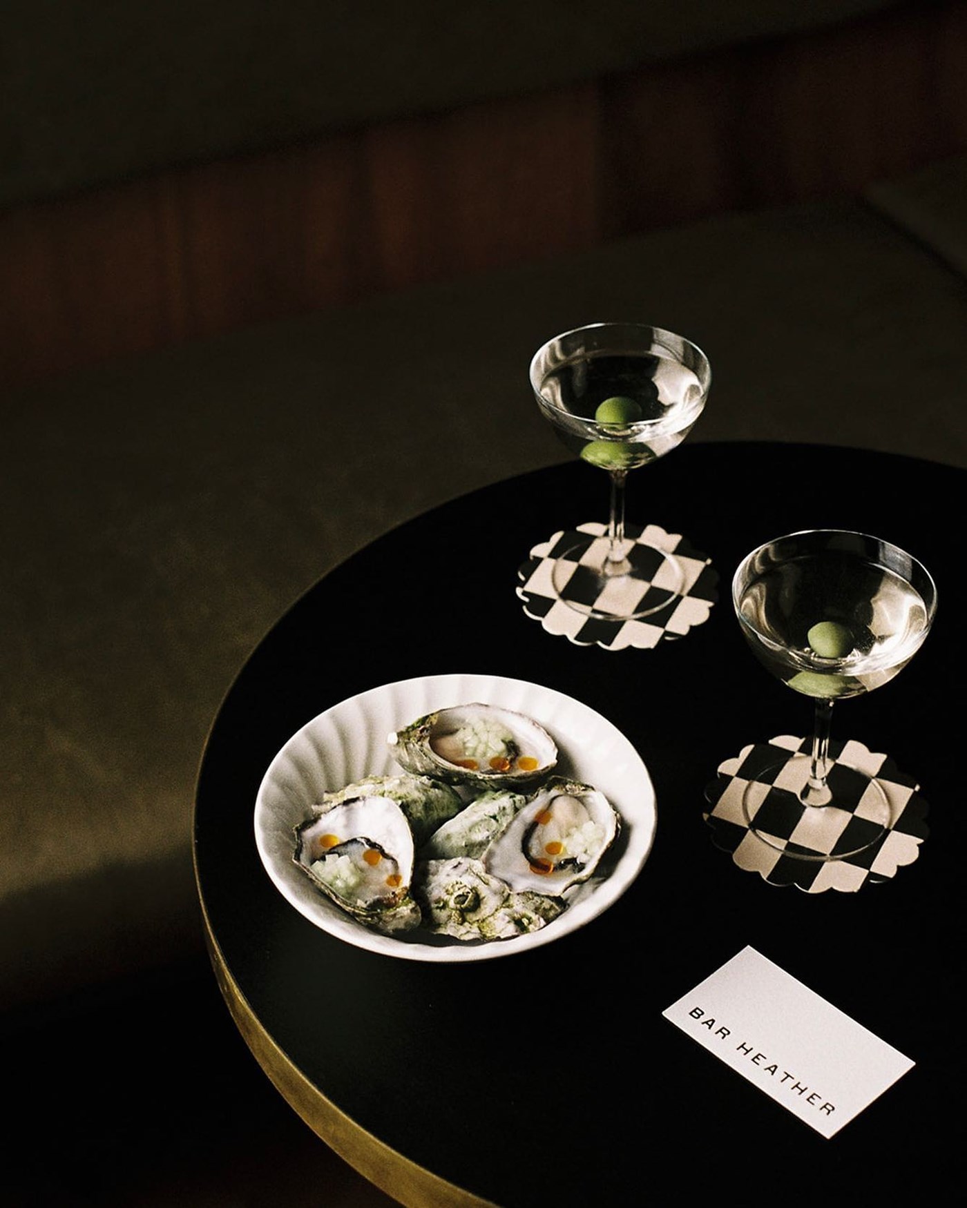 Two martinis and a plate of fresh oysters on a black table at Bar Heather
