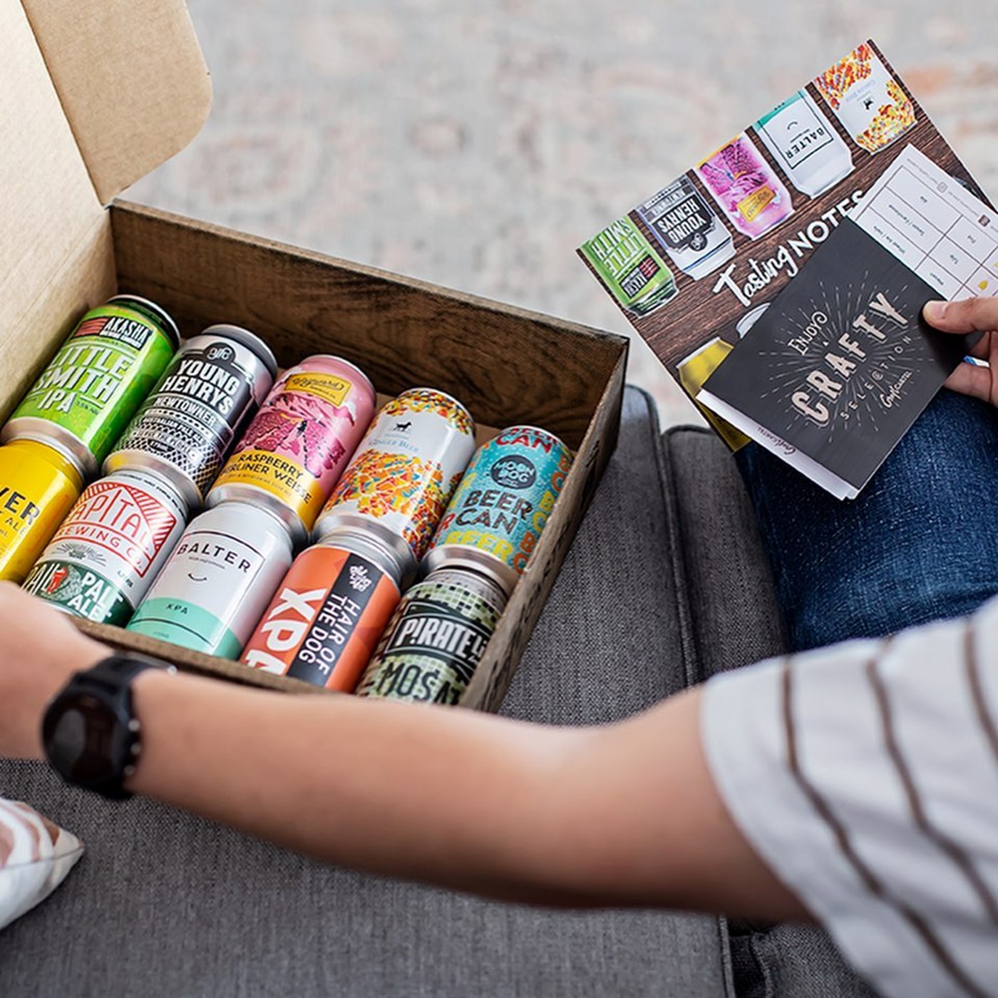 Someone unboxing a craft beer delivery on a grey couch 