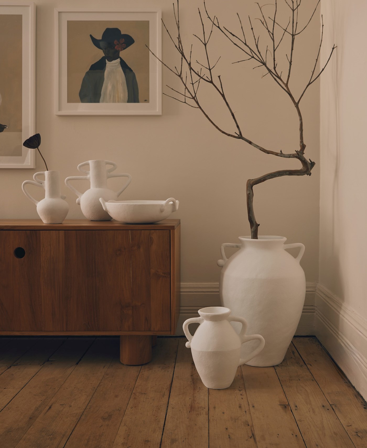 A cosy corner of a room with two white urn shaped terracotta pots, one of which is holding a large branch 