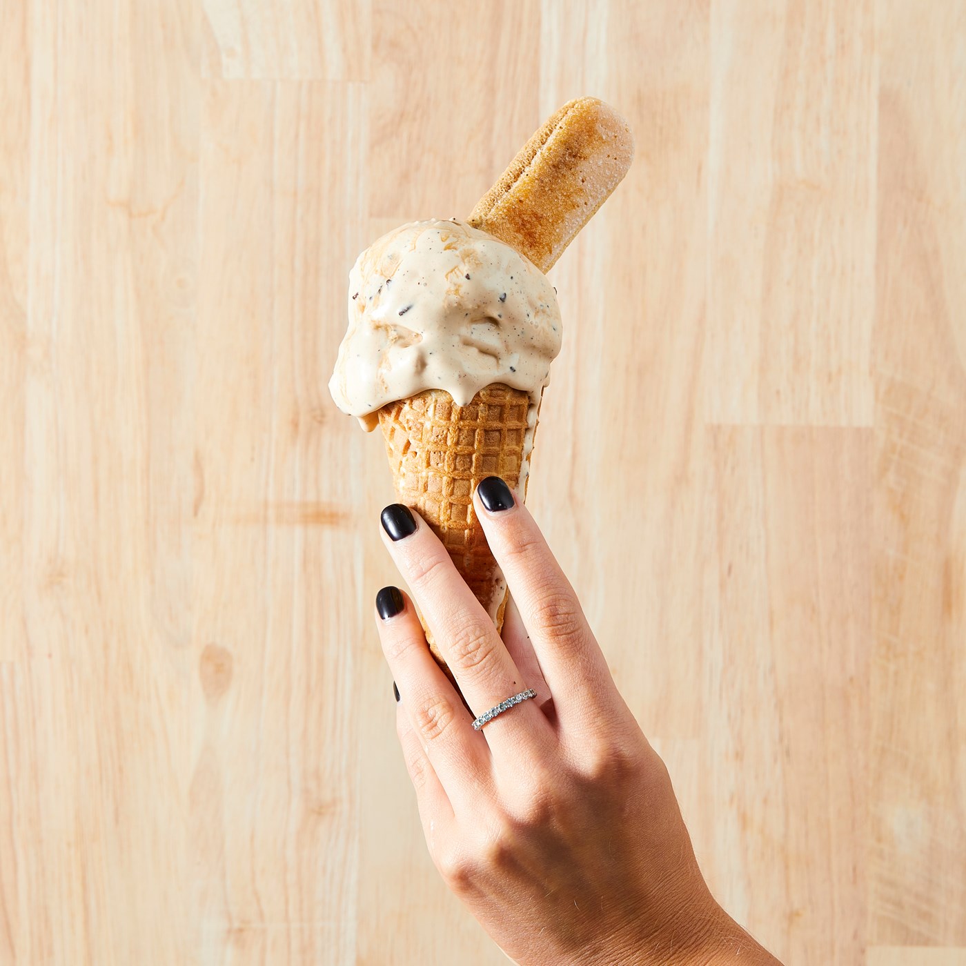 A hand with black-painted nails holds up a scoop of gelato.