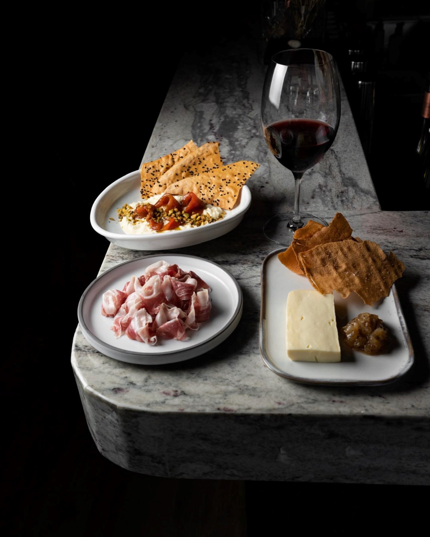 A moody bar, with charcuterie meats and cheeses served on the corner with a glass of red wine