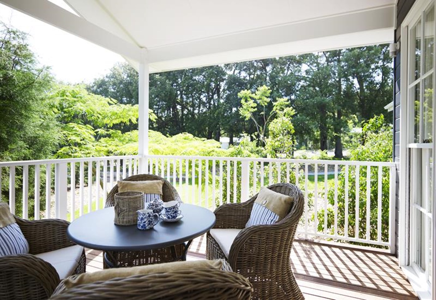 A terrace area with table and chairs and white balistrade surrounded by lush greenery at Bells at Killcare Palm Beach NSW