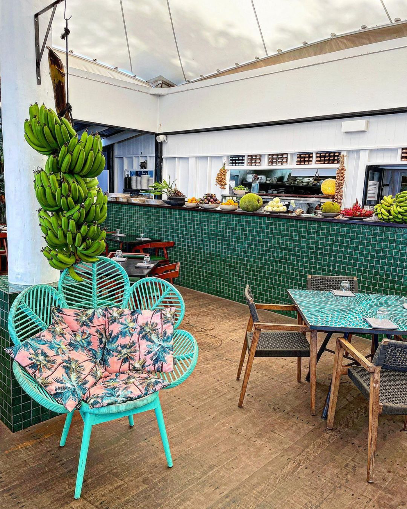 A green tiled bar stacked with fruit, and dining tables in the foreground