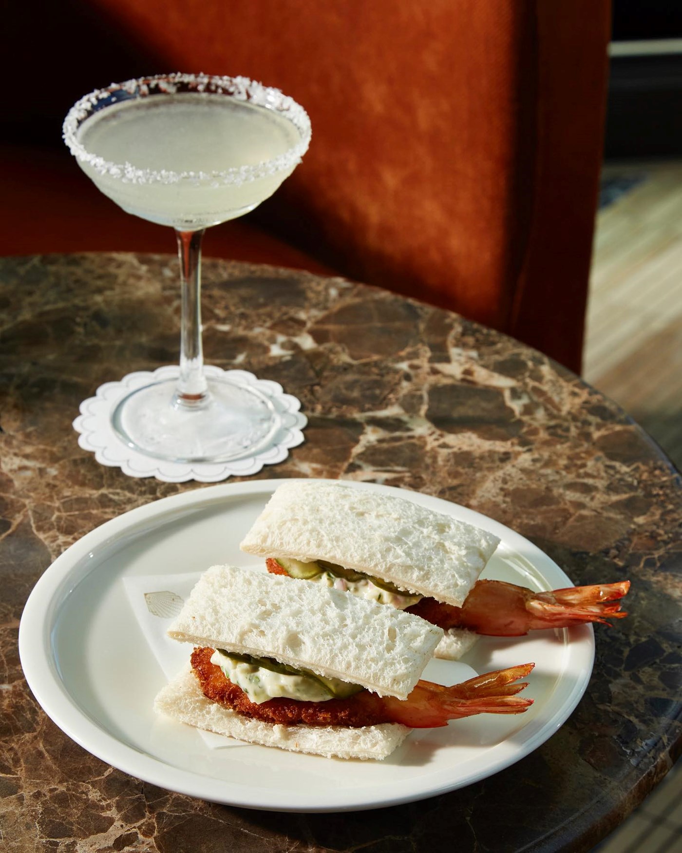 Two whole prawn crustless sandwiches and a margarita sitting atop a smokey marble table 