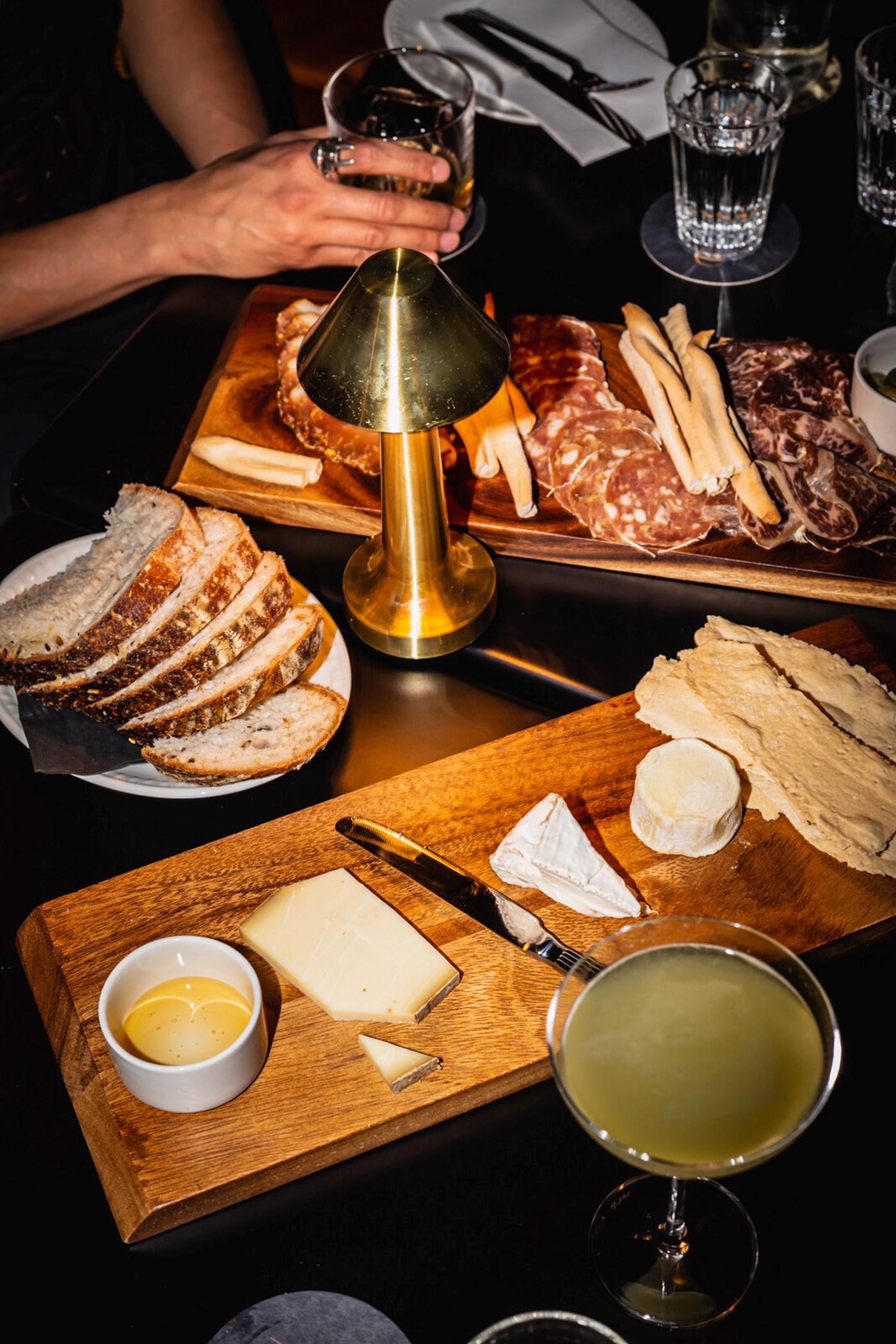 A top down view of a low lit table with cheeses and charcuterie and cocktails on top at Bar 1880