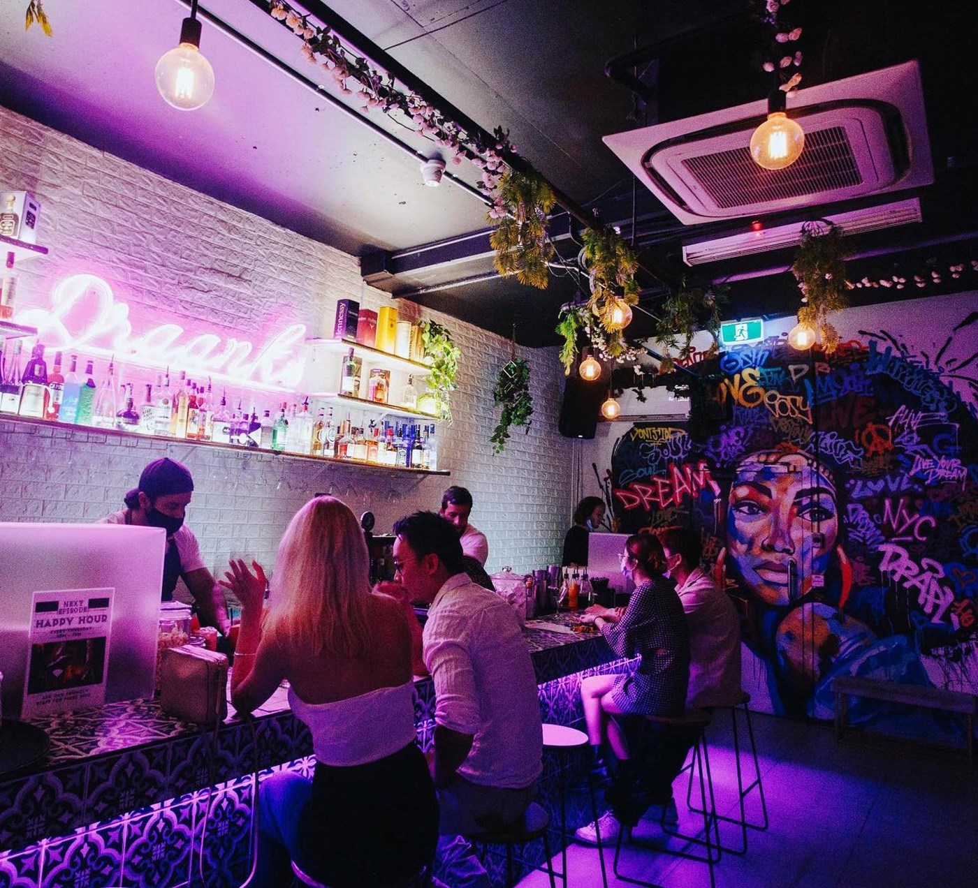A moody bar with graffitied walls, customers seated at the bar