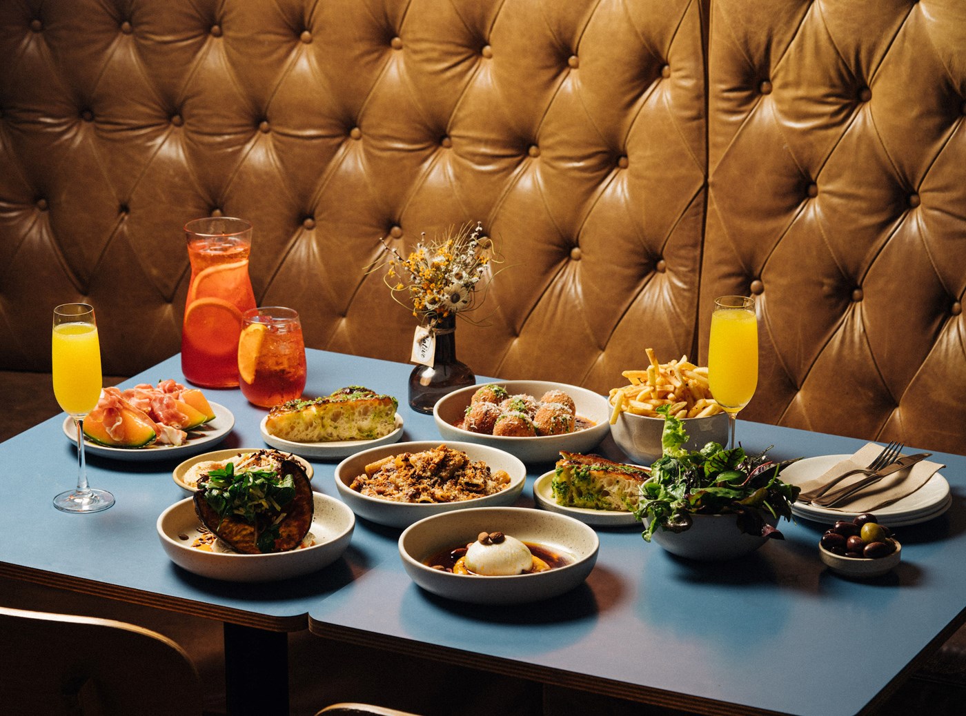 A blue laminate table full of cocktails and assorted dishes against a brown leather booth 
