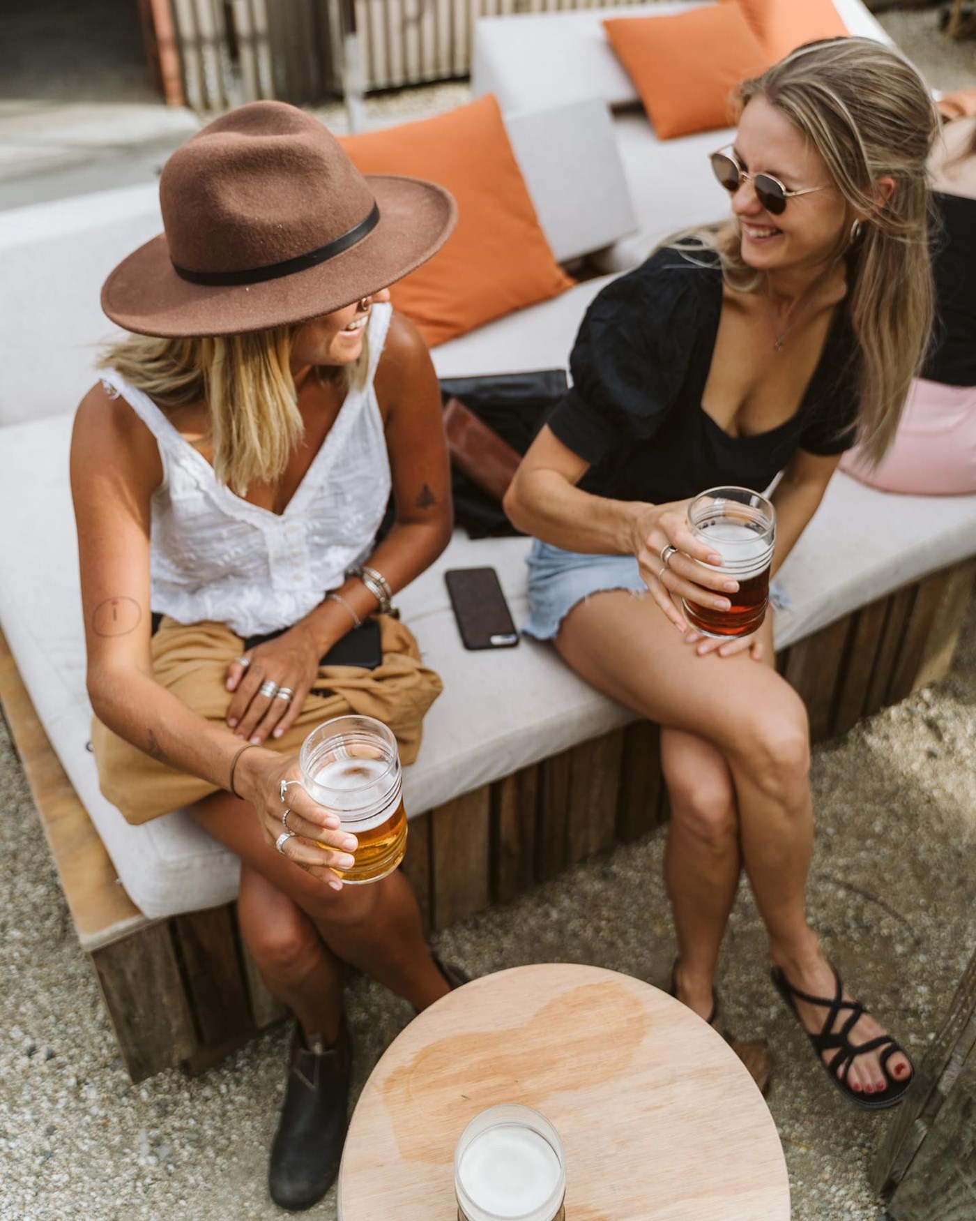 Two ladies sitting on a plush bench enjoying a beer 