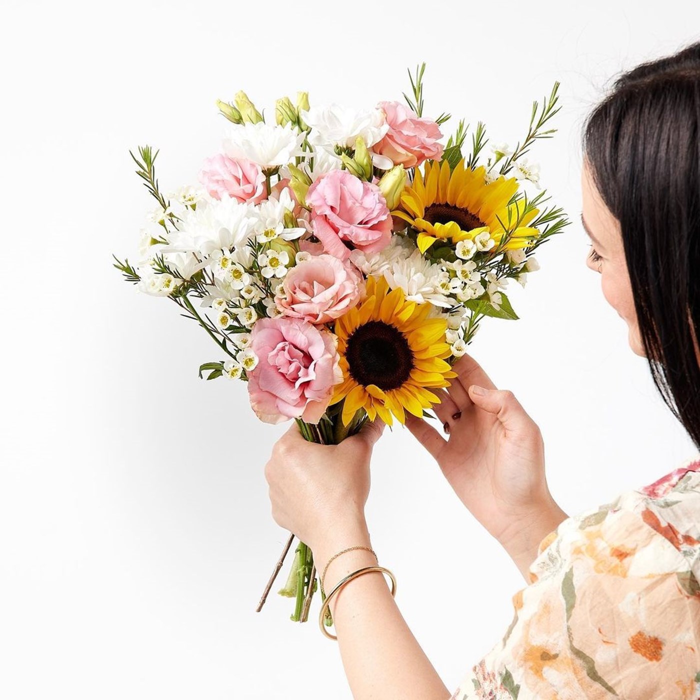 A woman holds a bouquet of flowers, made up of roses, sunflowers and daisies. 