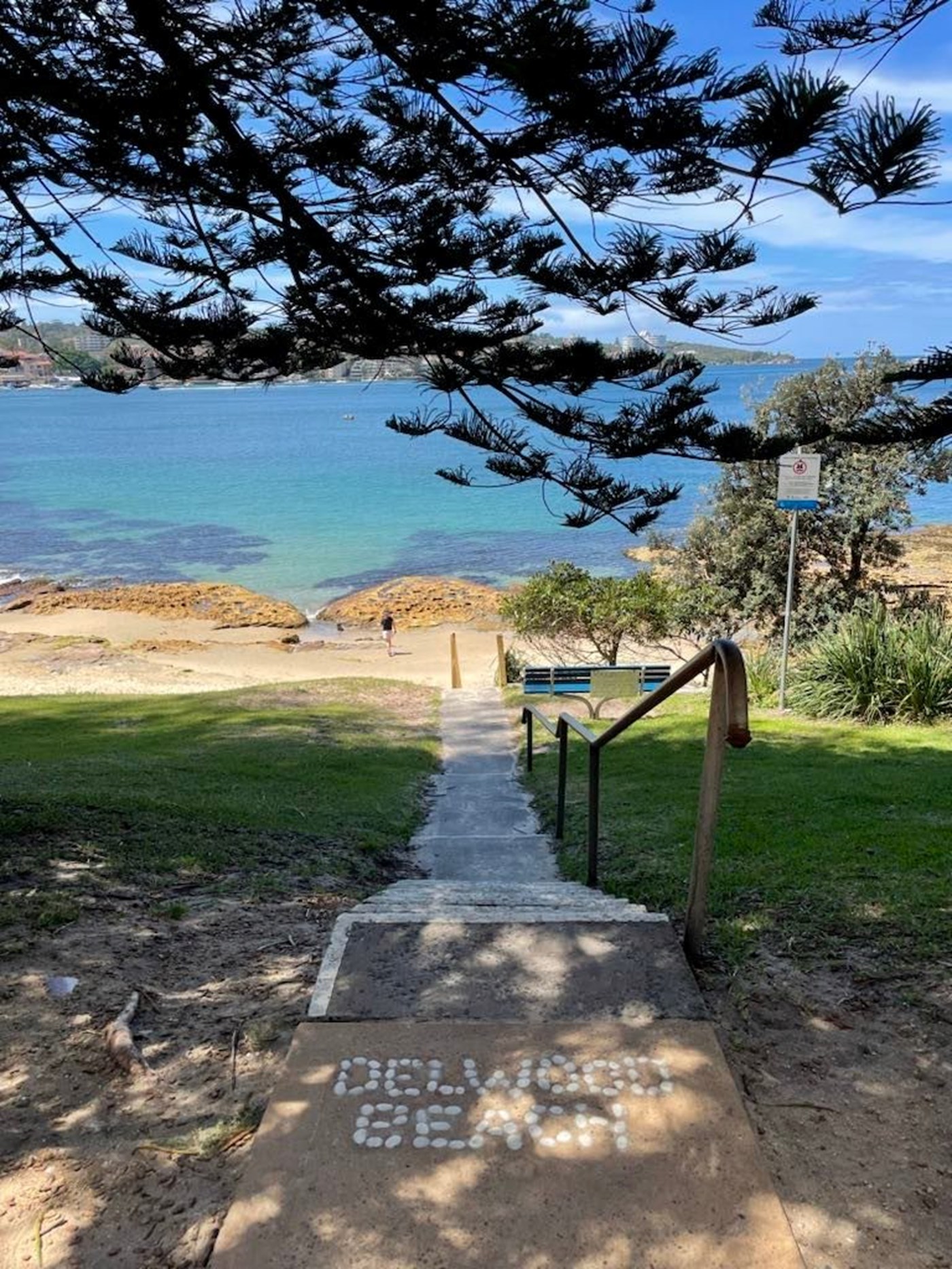 A narrow staircase snakes down to the water at Delwood Beach. At the top, the words 'Delwood Beach' are spelled out in stone.