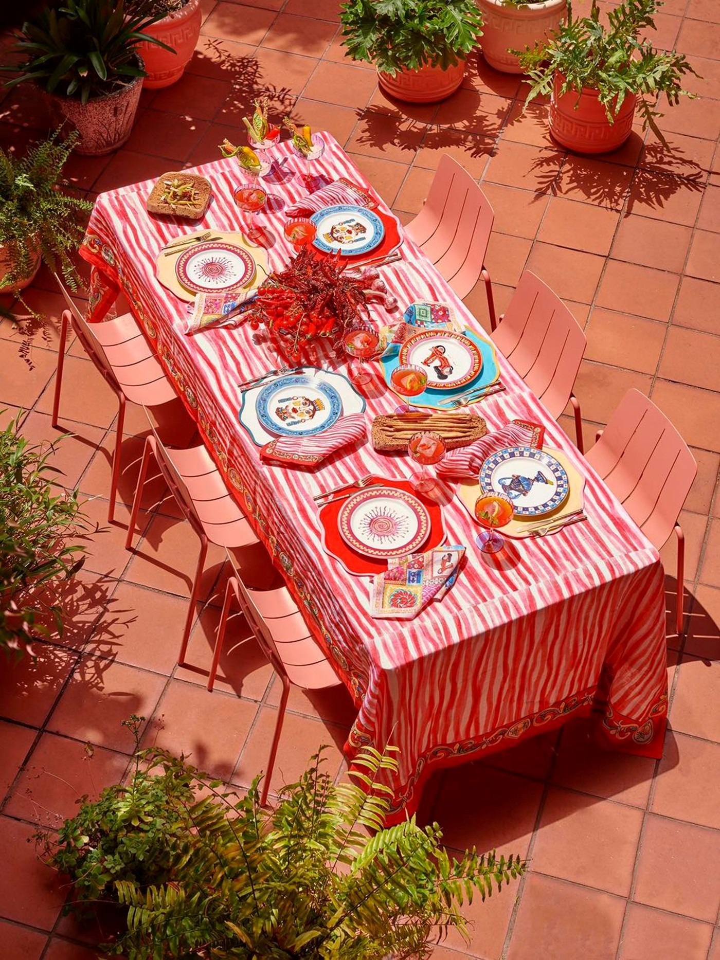 A top down view of a colourful set outdoors table complete with red and white table cloth against terracotta floor tiles 