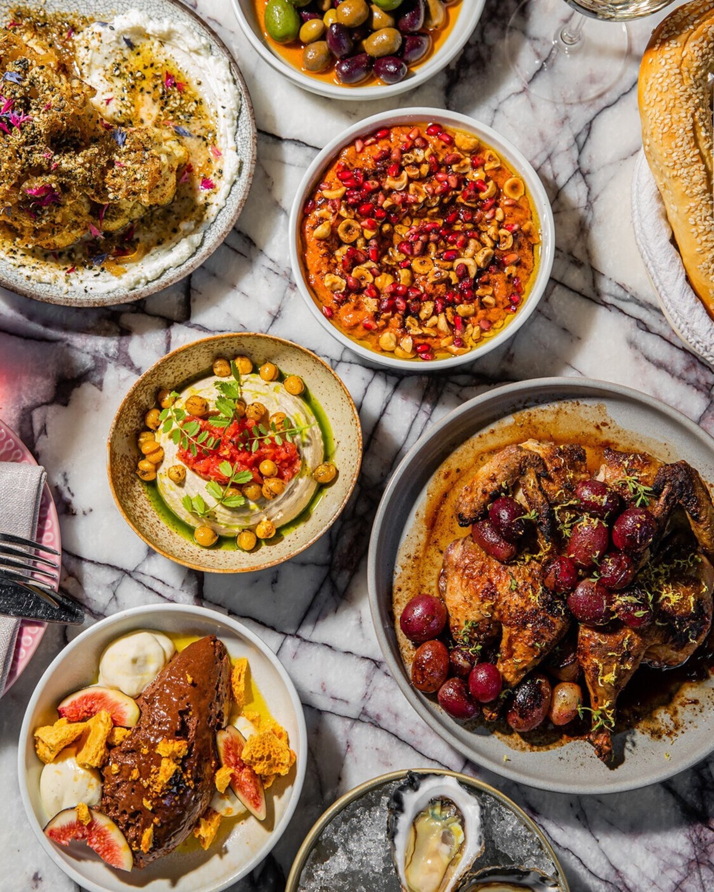 A marble table topped with vibrant Middle Eastern dishes including chicken and olives, ice cream, hummus and oysters 