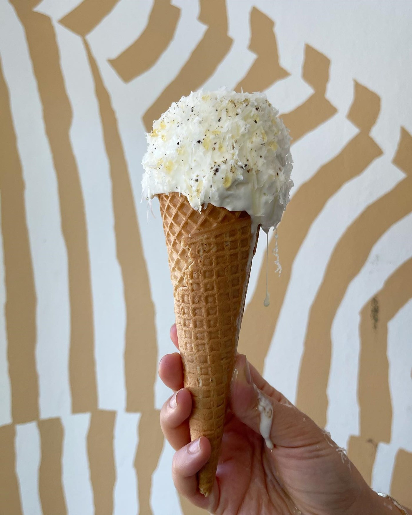 A scoop of dripping gelato is displayed against a striped wallpaper. 