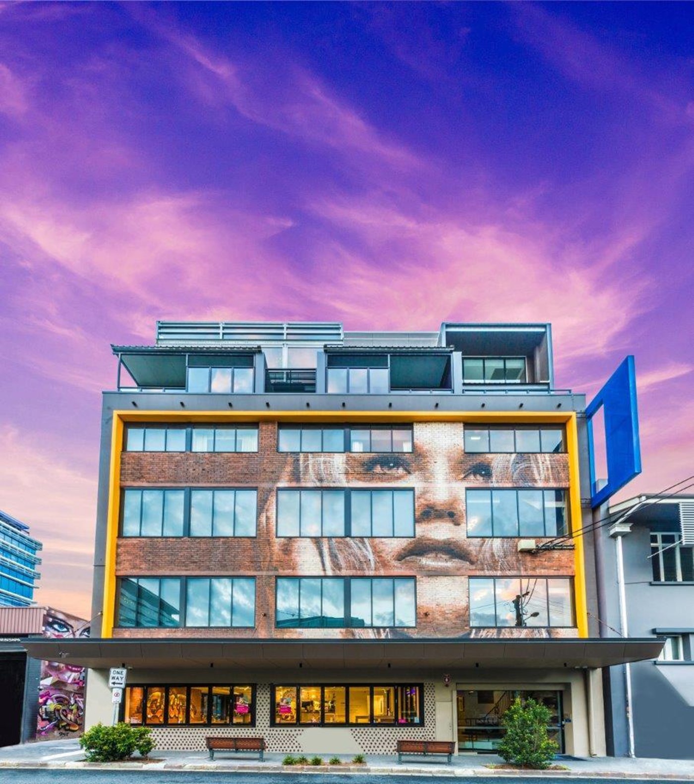 Exterior of a brick hotel with a mural of a face painted over it
