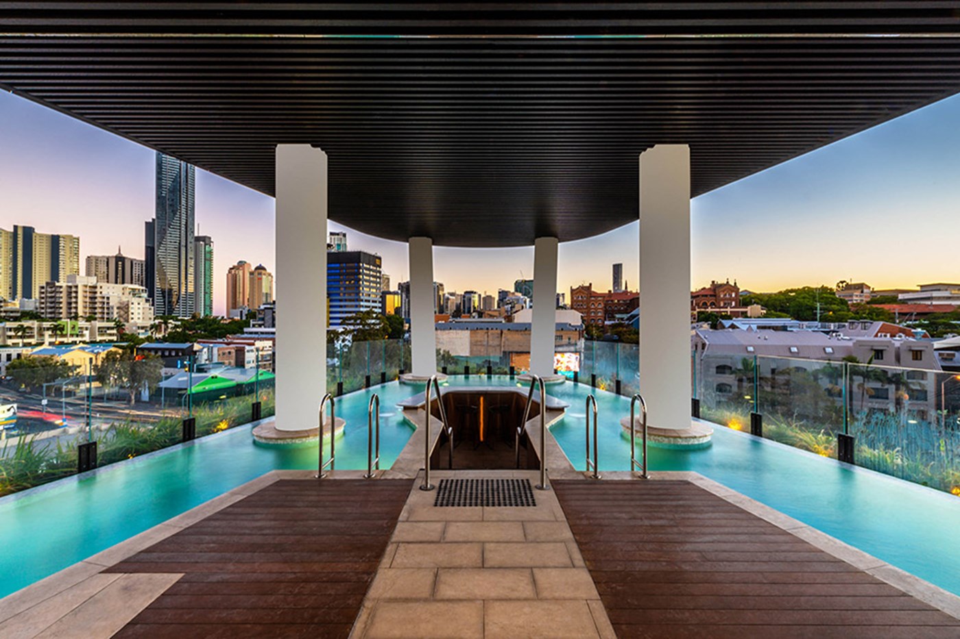 An infinity pool on a rooftop with large white pillars, surround by views of the city skyline.