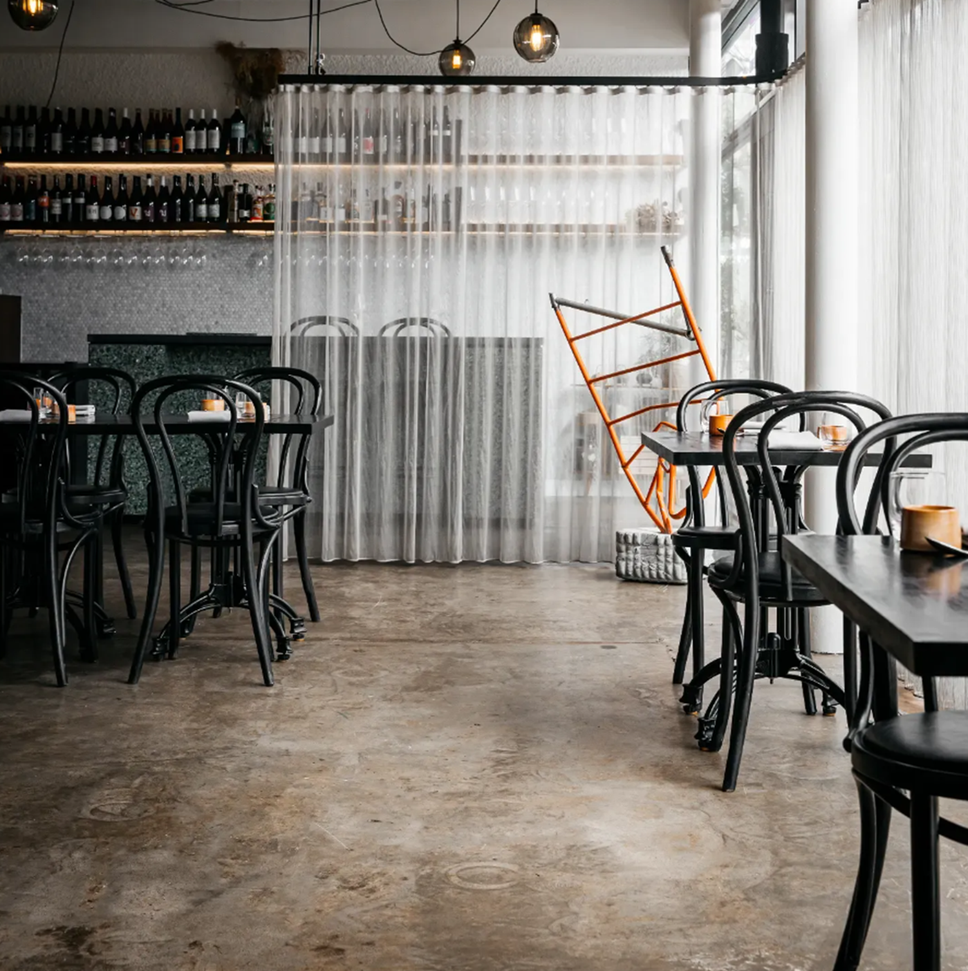A monochrome and sleek restaurant with a polished concrete floor and a sheer curtain halfway across the bar 
