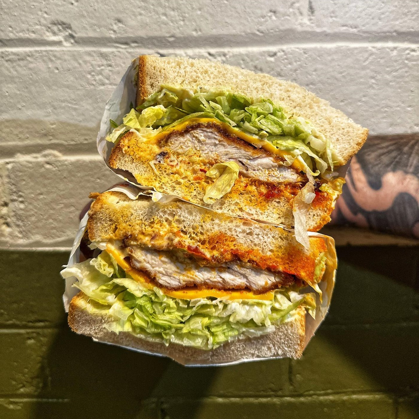 a cross section of Schnitzel Sandwich with white brick wall background Self Raised Bread Shoppe Carlton Sydney