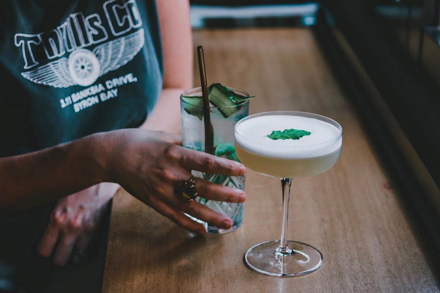 A hand reaching for one of two cocktails on a brown bar table