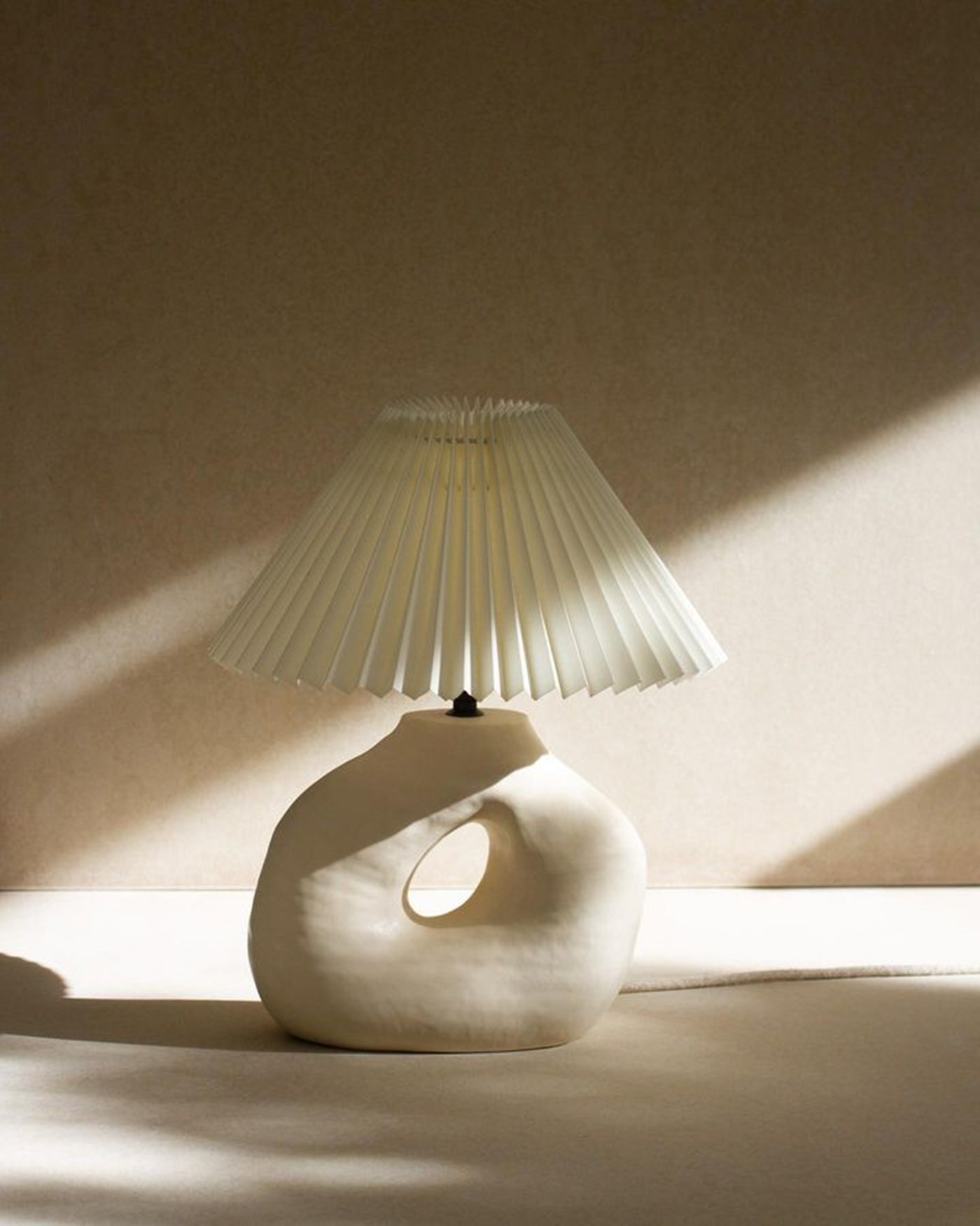 A handcrafted ceramic lamp with fluted shade sitting in dappled sunlight 