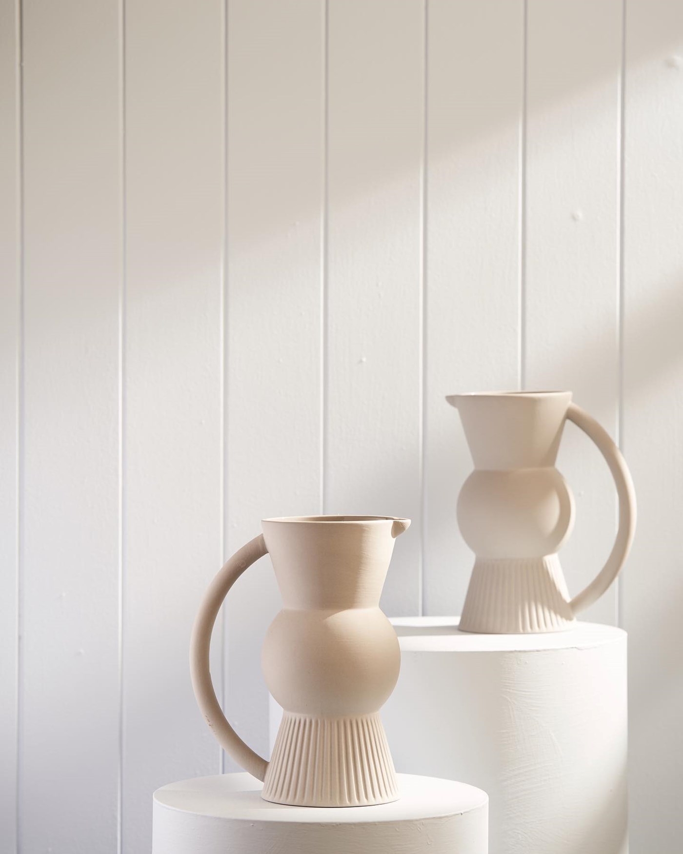 Two sculptural white ceramic jugs from Robert Gordon sitting on circular plinths 