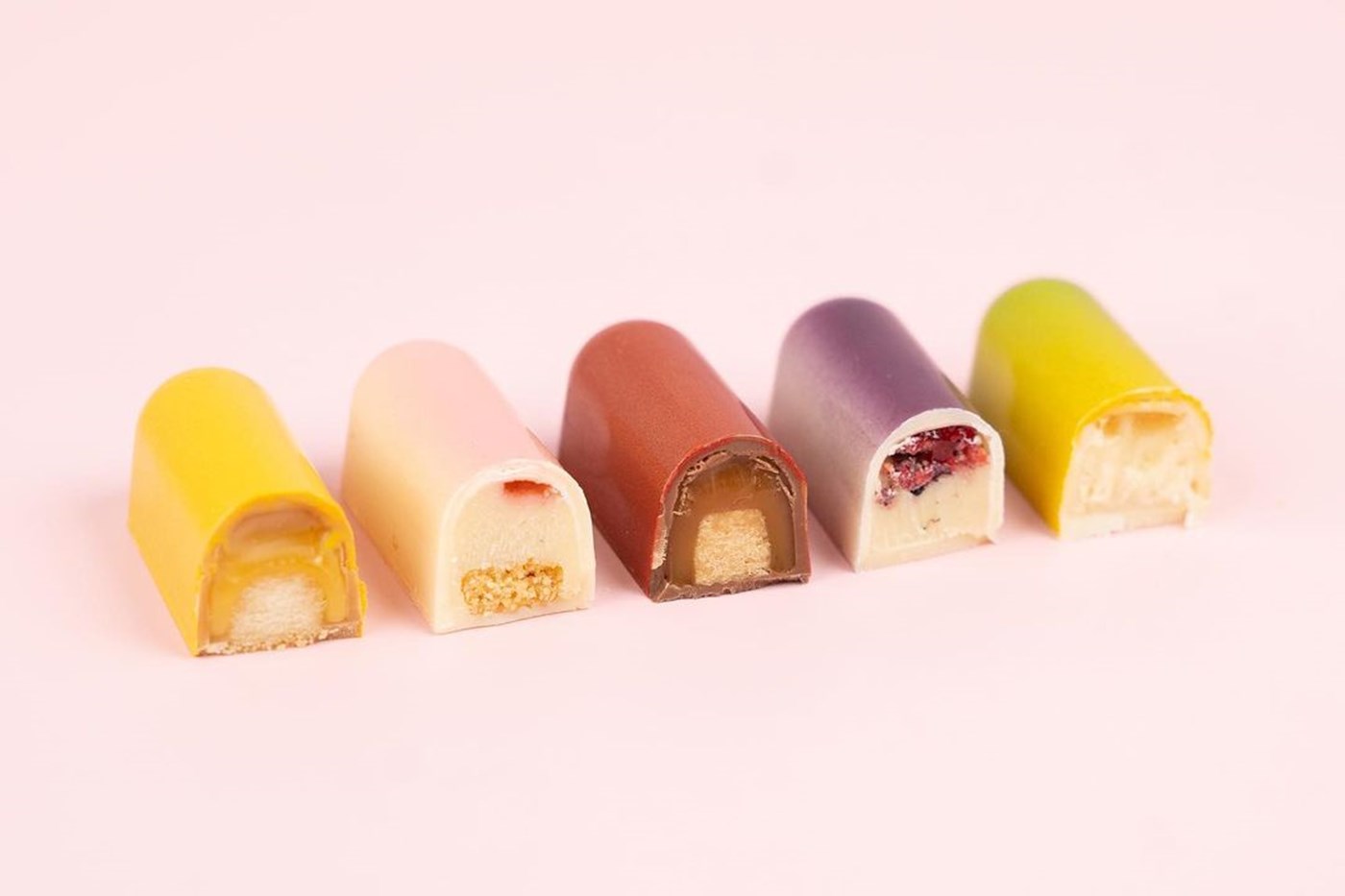 A pink background with five domed pastel truffles lined up, each showing a cross section. 
