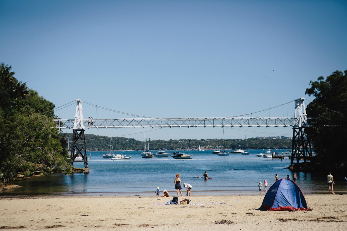 The large bridge runs across the beach at Parsley Bay as people play on the foreshore. 