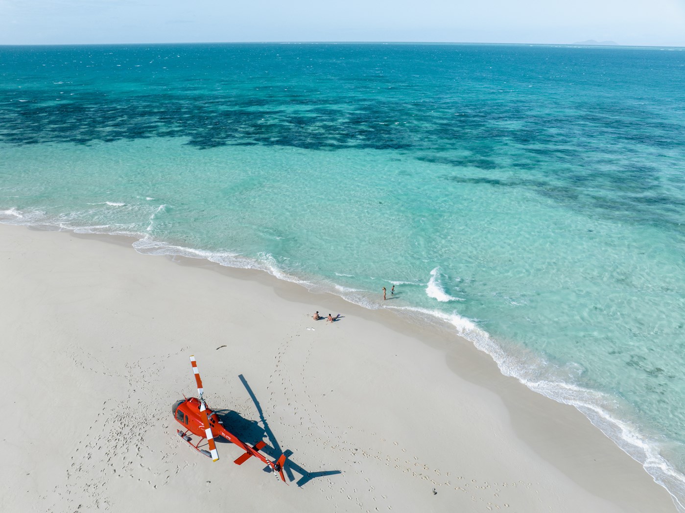 A bright red helicopter on a white sand cay surrounded by crystal clear blue water