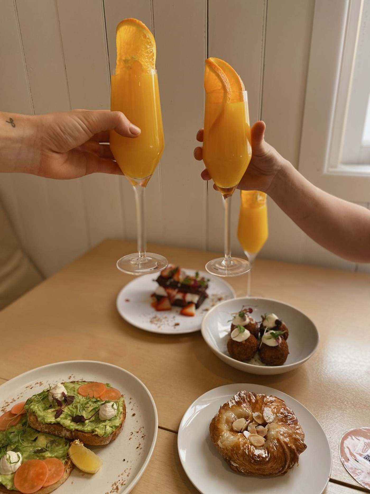 Breakfast plates with hands holding mimosa in a cheers at Plant Vibes vegan cafe Brisbane