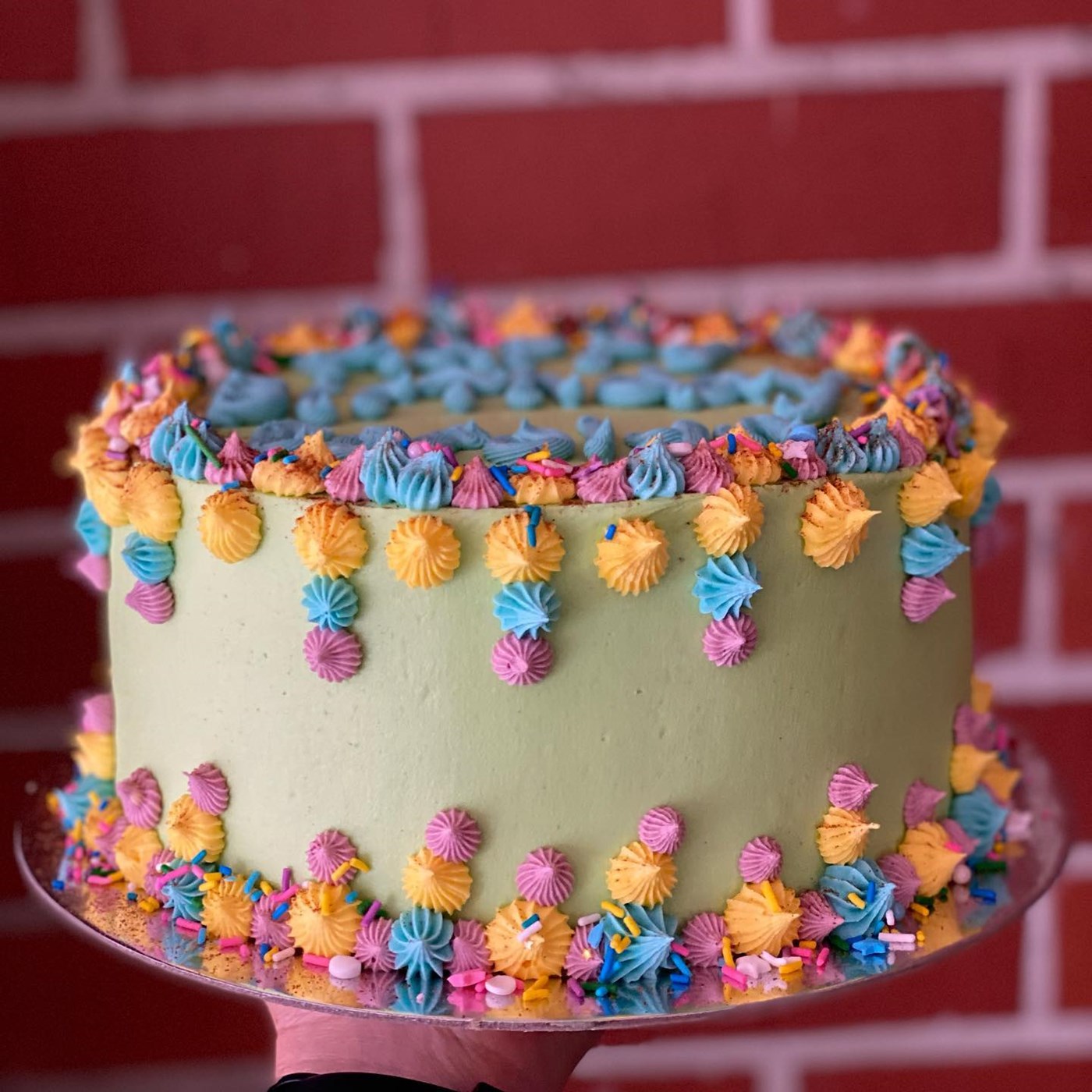 A cream caked with small purple, orange, blue and pink decorations piped all over. From Sweet Bones Bakery & Cafe